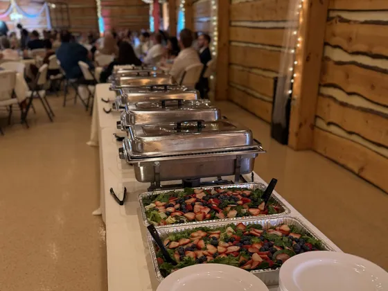 A 12Eleven Catering buffet line of chafing dishes and strawberry salad set up in a barn reception venue