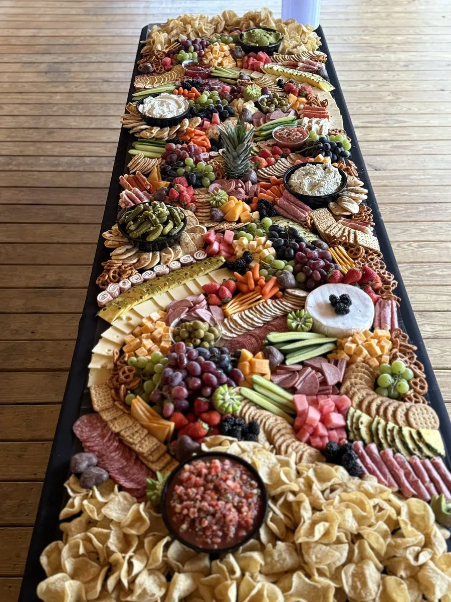 A grazing table laid out on a black runner with a pineapple centerpiece, brie, tortilla chips and salsa