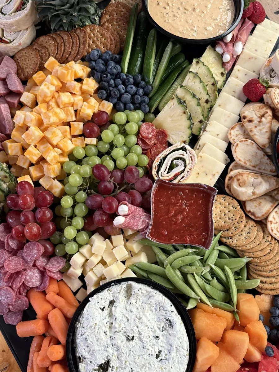 Overhead view of cubed cheeses, blueberries, grapes, salami roses, pita and dips on a grazing table
