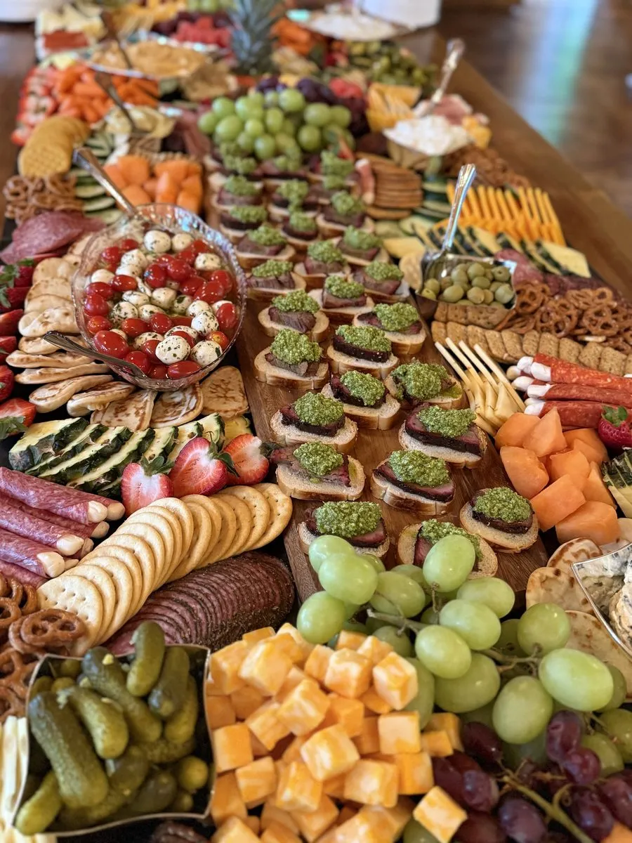 Crostini topped with pesto and beef alongside marinated mozzarella, grapes and cubed cheddar on a grazing table