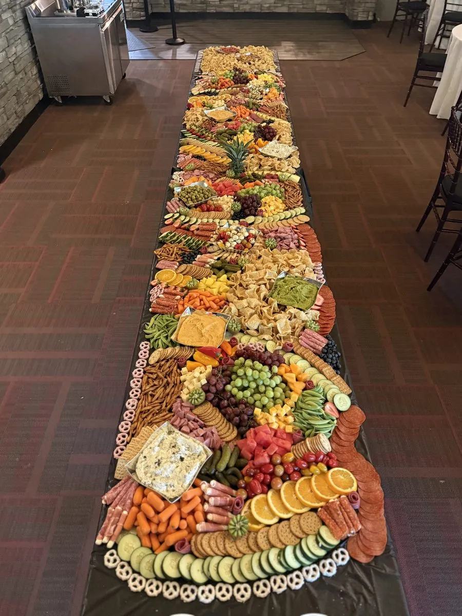 A grazing table running the full length of a reception hall, loaded end to end with cheeses, cured meats, fruit and crackers
