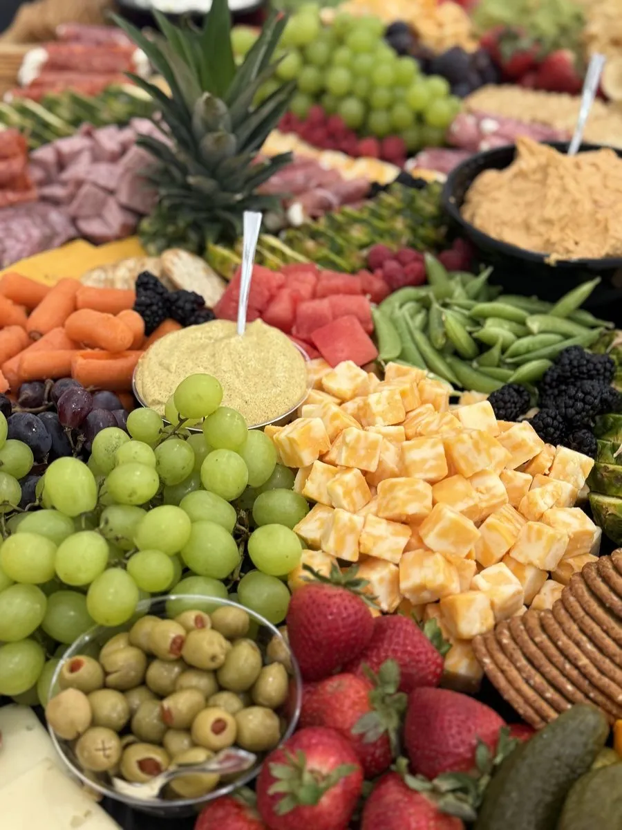 Close-up of cubed cheddar, green grapes, olives, snap peas and baby carrots on a grazing table