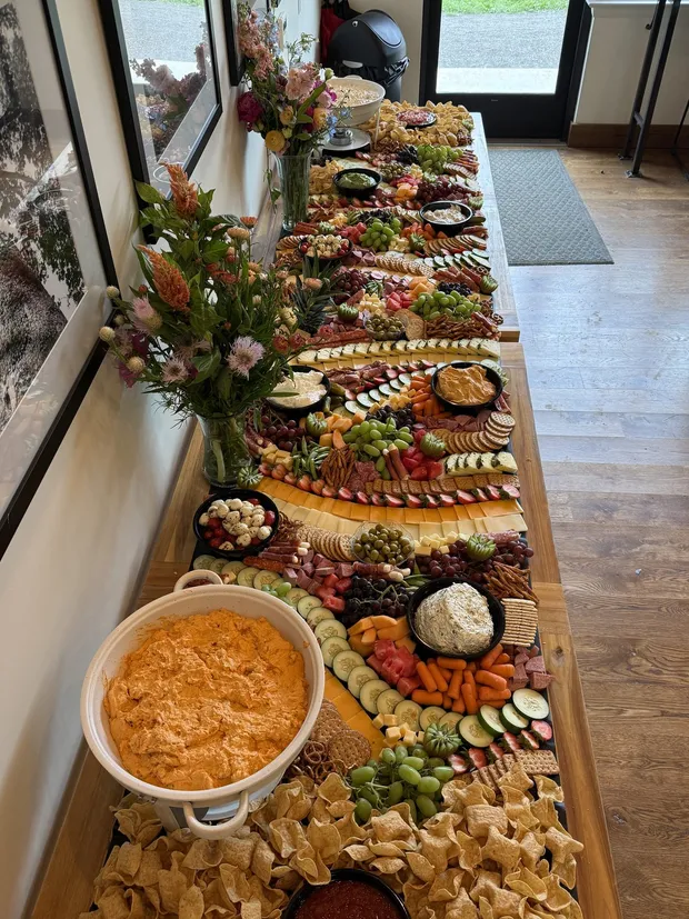 A long 12Eleven Catering grazing table loaded with cured meats, cheeses, fresh fruit, vegetables and crackers