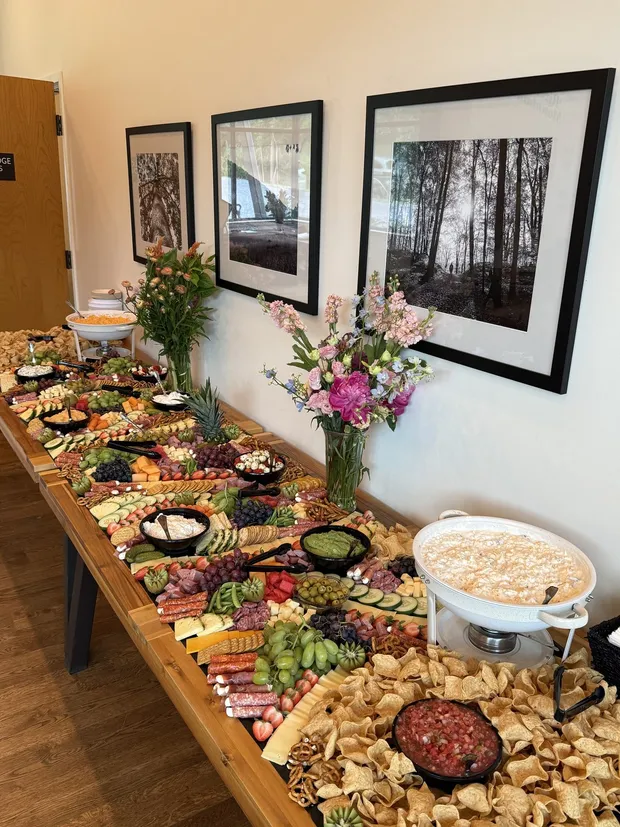 A grazing table of cured meats, cheeses, fruit and crackers set with fresh flowers for a wedding cocktail hour
