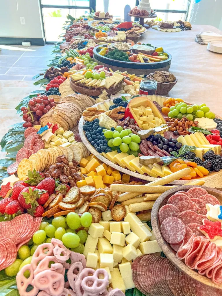 A grazing table of sliced cheeses, salami, strawberries, grapes and yogurt pretzels set for a cocktail hour