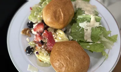 A guest's plate of dinner rolls, strawberry walnut feta salad and Caesar salad at a 12Eleven Catering buffet