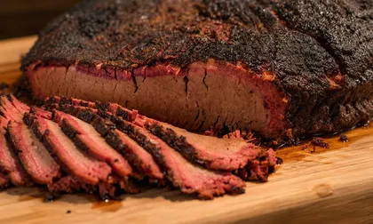 Sliced smoked beef brisket with a dark peppery bark on a wooden board