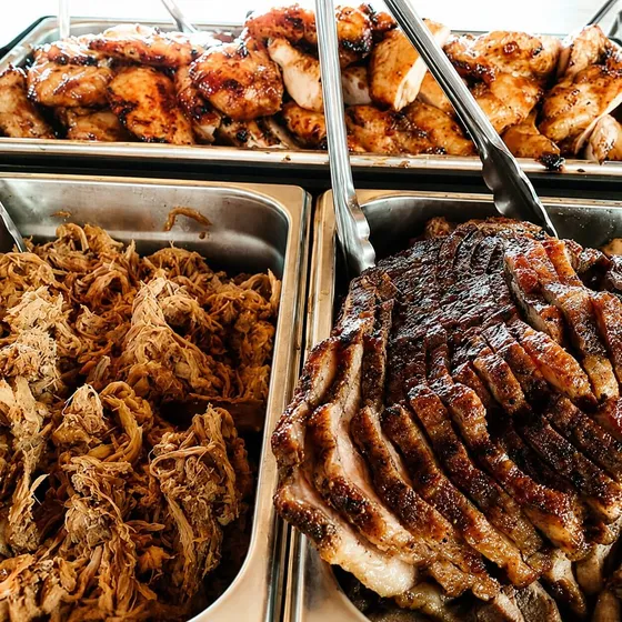 Chafing pans of freshly smoked ribs, pulled pork and chicken on a 12Eleven Catering buffet line
