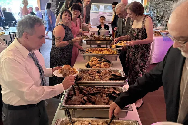 Wedding guests serving themselves from a 12Eleven Catering buffet line of smoked brisket, pulled pork, macaroni and cheese and dinner rolls