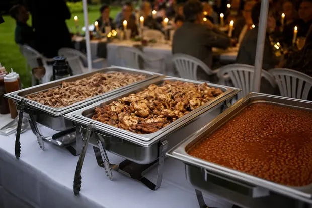 Outdoor wedding reception buffet line set with chafing dishes at dusk under string lights